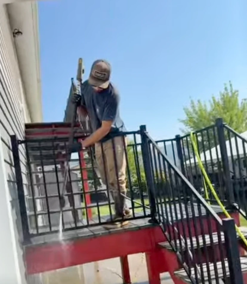 Technician pressure washing a metal stair railing on a commercial landing